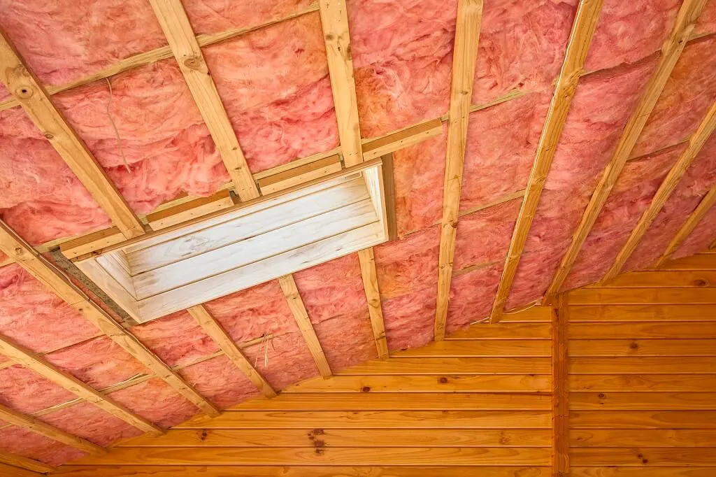Pink fiberglass insulation installed between attic rafters around a skylight shaft